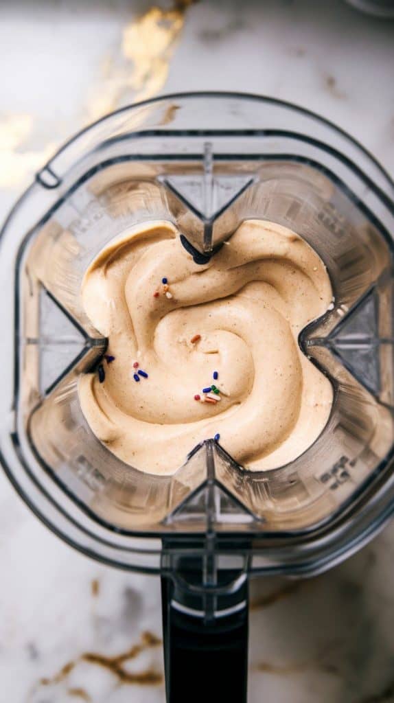 a blender mid-blend, the vanilla cake batter smoothie swirling into a smooth, thick mixture with tiny flecks of sprinkles visible