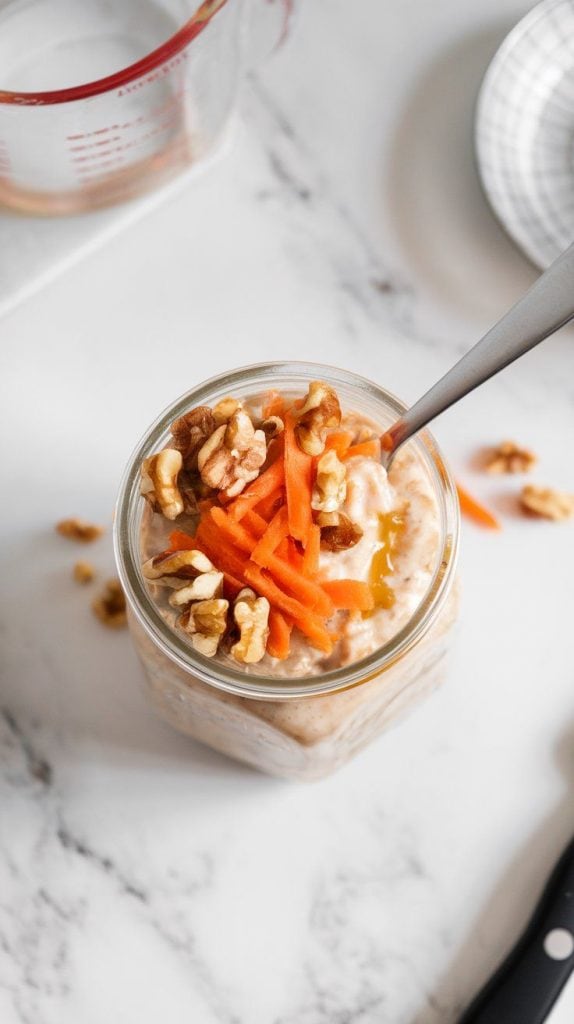 a glass jar of Carrot Cake Overnight Oats topped with chopped walnuts, fresh shredded carrot, and a drizzle of honey