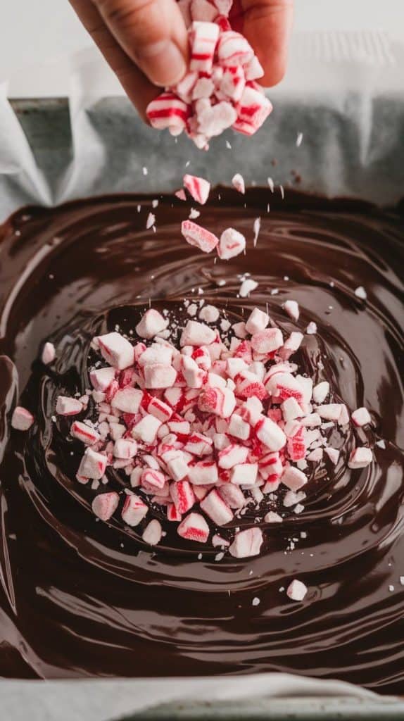 A super close-up shot of crushed peppermint candies being sprinkled over glossy chocolate fudge