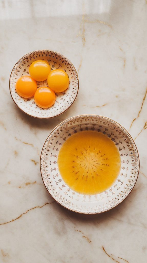 three eggs cracked open, with yolks in one small plate and egg whites in another