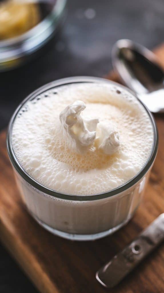 A super close-up, top-down shot of a hand mixer whipping thick, fluffy coconut cream in a small glass bowl