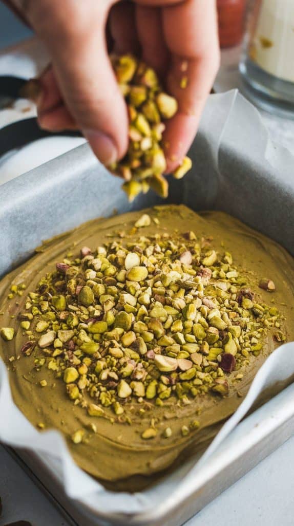 A super close-up shot of crushed pistachios being sprinkled over the smooth fudge