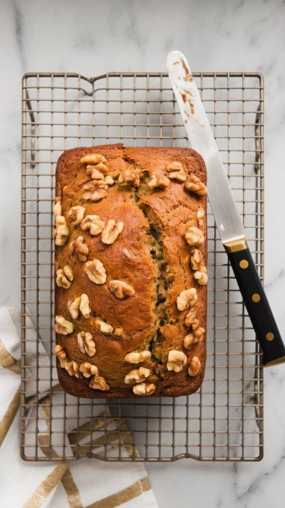 a freshly baked loaf of Zucchini Banana Nut Bread resting on a cooling rack, with a knife cutting into the golden, moist texture